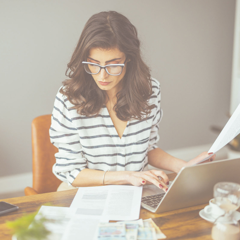 Photo d’une femme assise à un bureau qui travaille sur son ordinateur portable en consultant des documents 